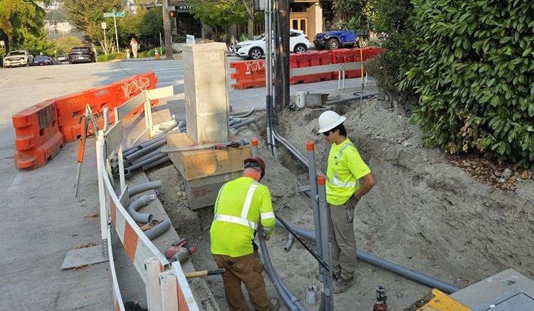 Image shows an area of sidewalks excavated on Eastlake Ave E with team members installing the infrastructure below the ground to house electrical wiring for signals. 