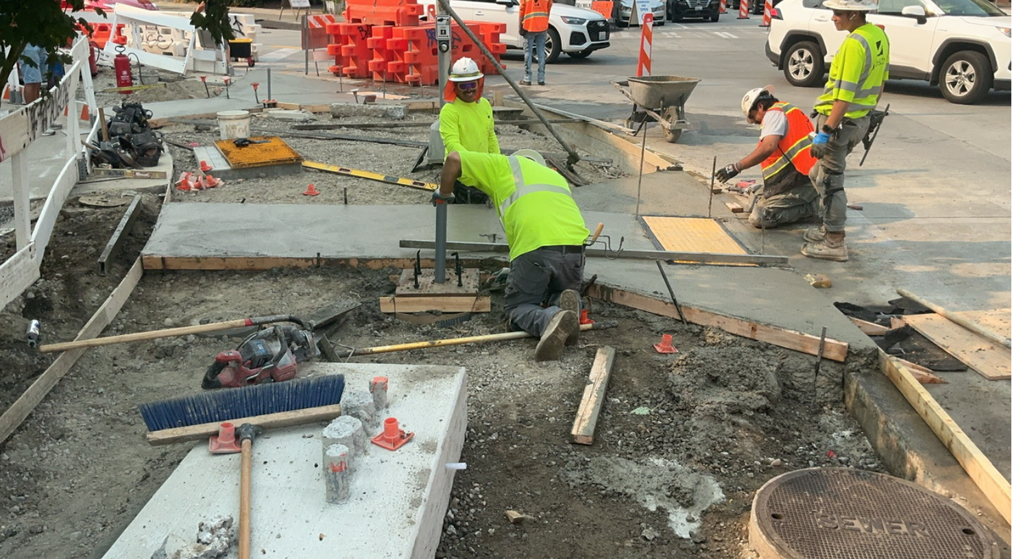Image shows crews smoothing out the concrete for a new accessible curb ramp.