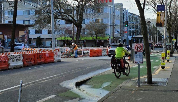 Image shows crews installing new sidewalks on the east side of Roosevelt Way NE. Traffic is shifted to the west side. 