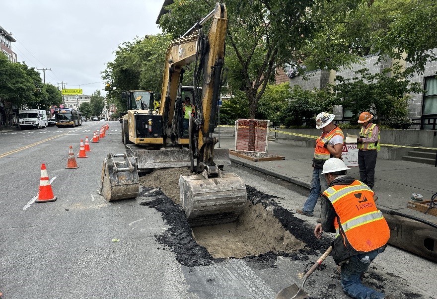 Crew members perform trenching work for new pipes and cables with the help of an excavator in the Ballard neighborhood