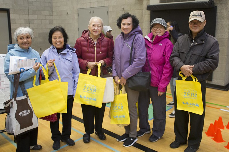 A group smiles while holding yellow Vision Zero tote bags at an SDOT community event.