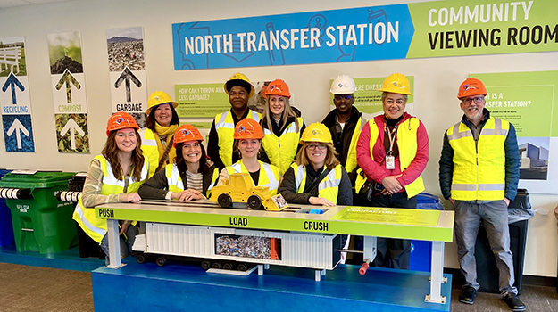 Members of the Solid Waste Advisory Committee, wearing hardhats and high-visibility vests, pose in the Education & Viewing Room of the North Transfer Station.
