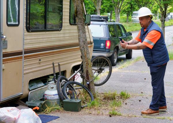 SPU employee taking a photo with phone of debris on sidewalk next to an RV.