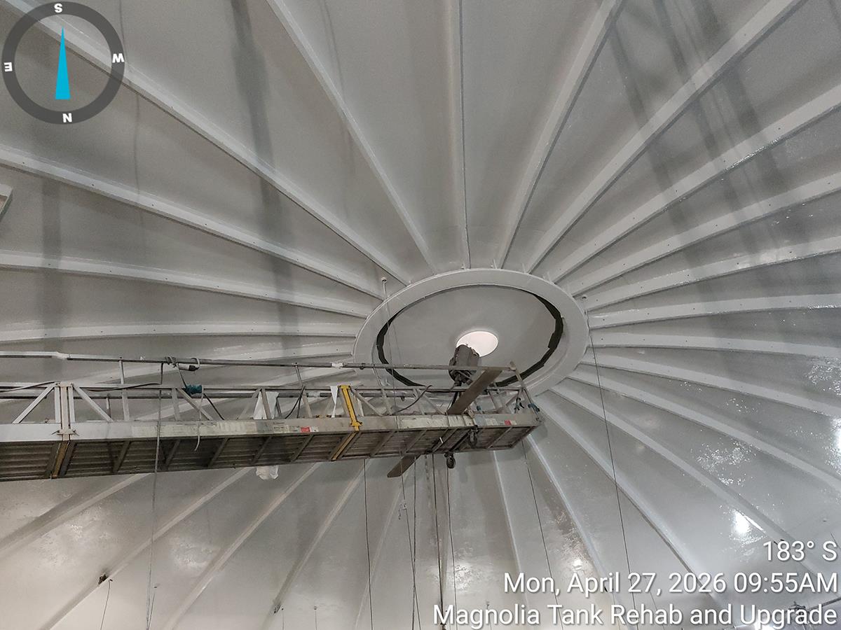 A section of metal scaffolding is positioned via a cable through a round hole in the center of a large domed roof. 