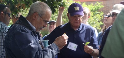 people watch as a man closely inspects a leaf.