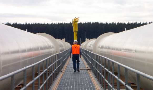 Worker in orange vest and hardhat walking between intake pipes.