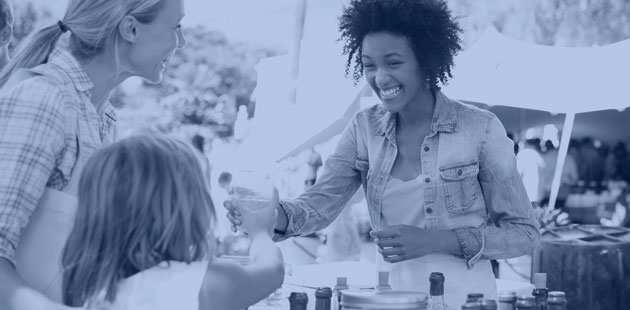 Farmers market vendor serving a beverage to a young customer