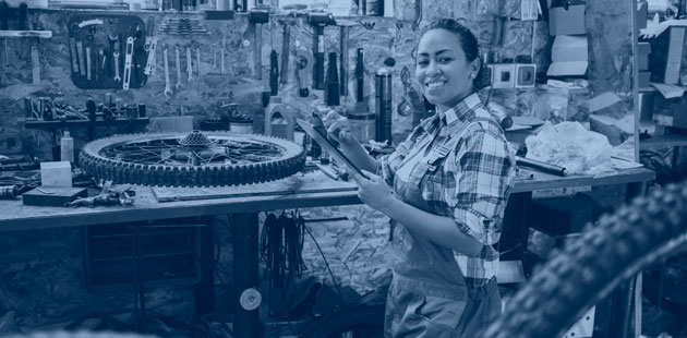A bicycle shop owner stands in her workshop with her tools, smiling.