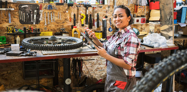 A bicycle shop owner stands in her workshop with her tools, smiling.