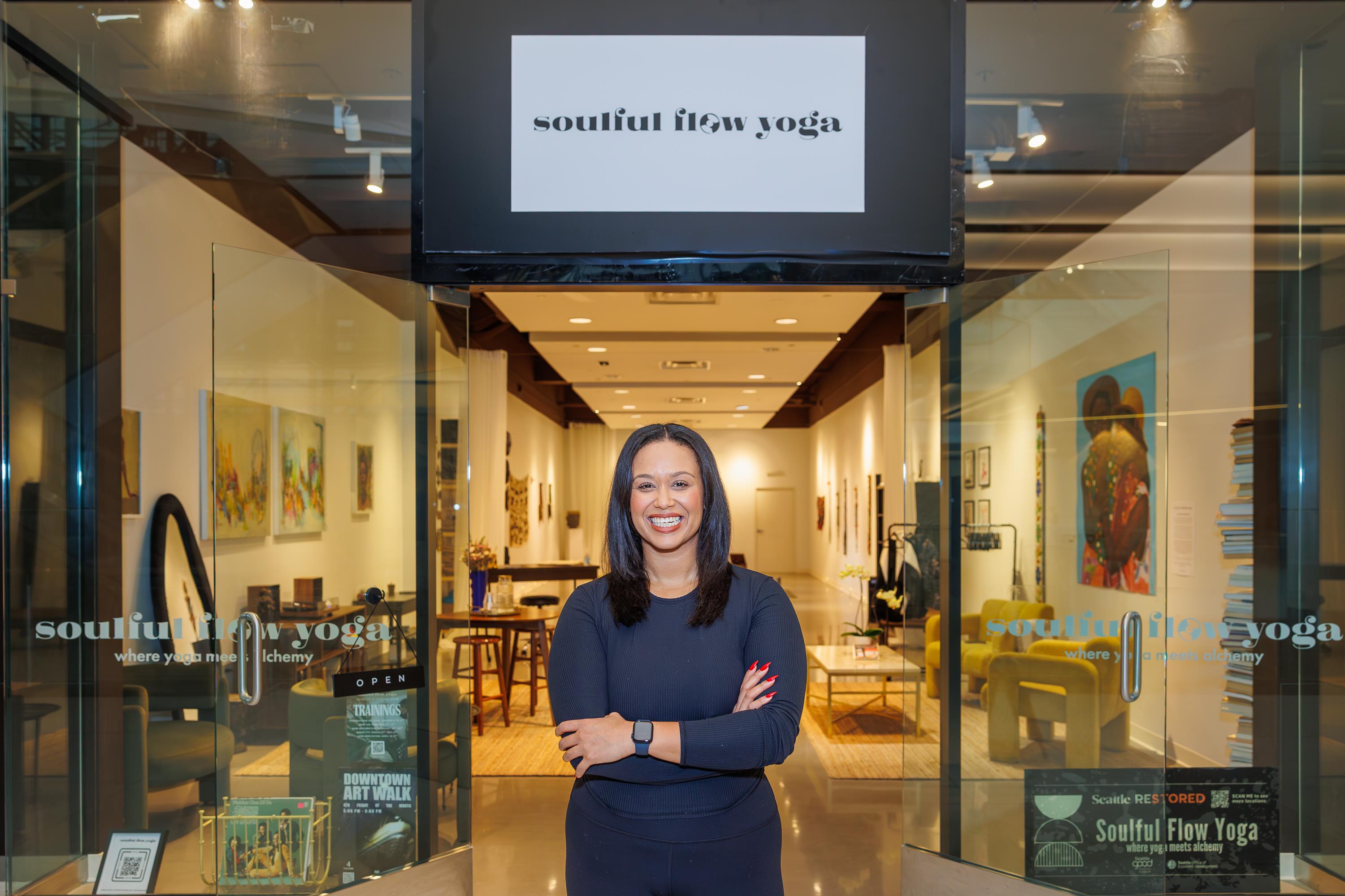A black woman stands in front of her yoga pop-up smiling and crossing her arms