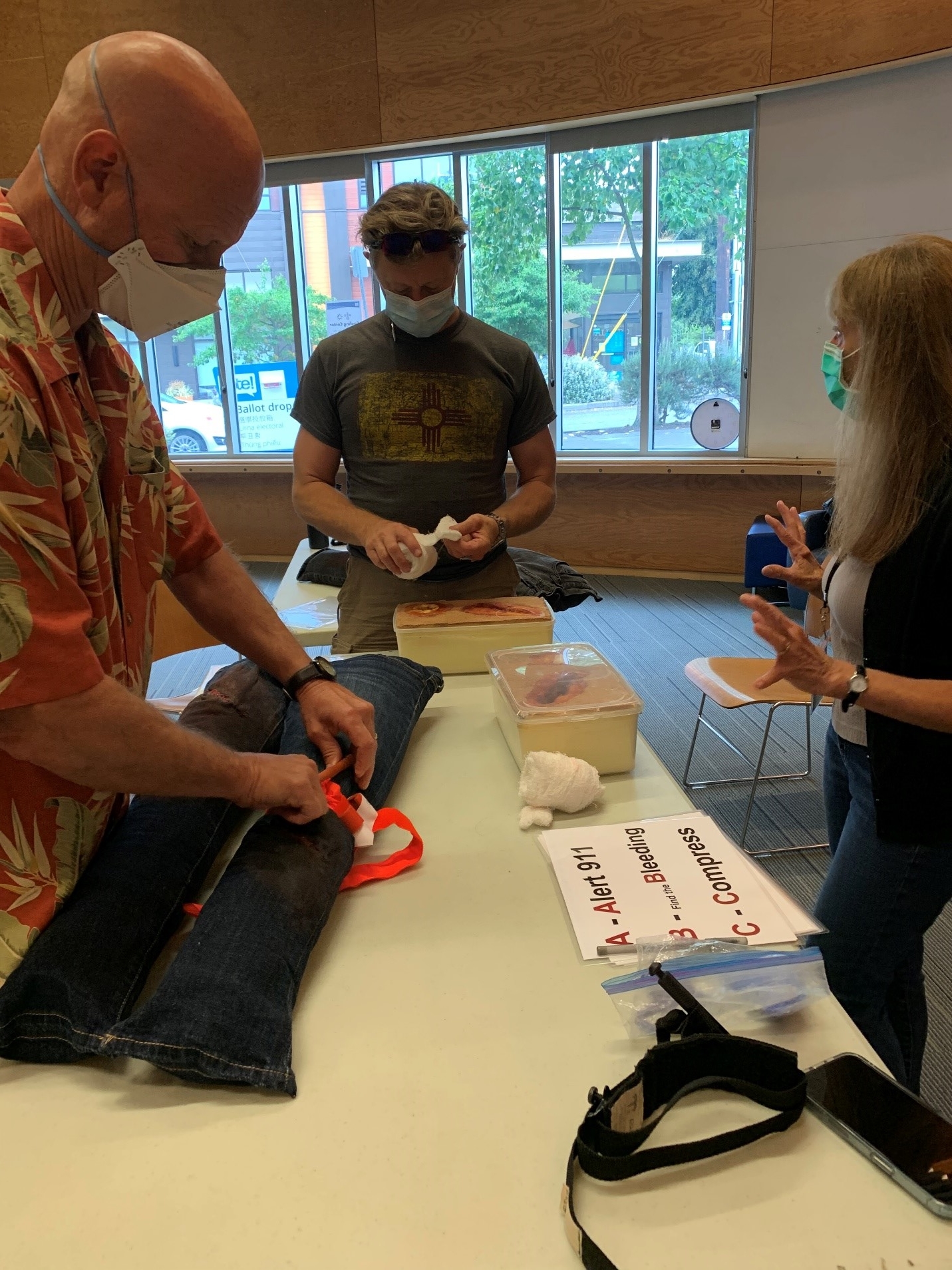 two people practicing stopping bleeding wound on practice legs with instructor providing instruction