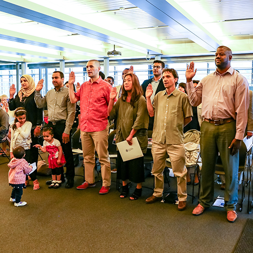 A multiracial group of new Americans taking the Oath of Allegiance in a brightly lit room in Seattle City Hall.