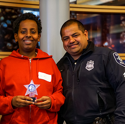 SPD Sergeant Adrian Diaz poses with an Immigrant Family Institute graduate youth. Both are smiling.