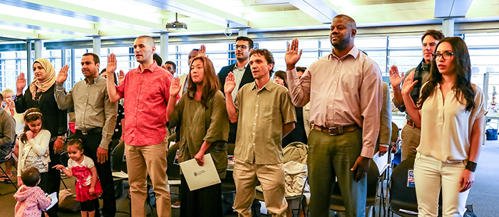 A multiracial group of new Americans taking the Oath of Allegiance at their Flag Day Citizenship Ceremony in a brightly lit room inside Seattle City Hall.