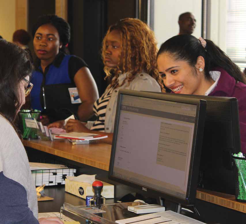 A miling resident of color with long hair at a counter talking to a customer service representative in the process of registering to vote.