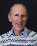 Andrew Danneberg smiling at the camera in front of a grey background