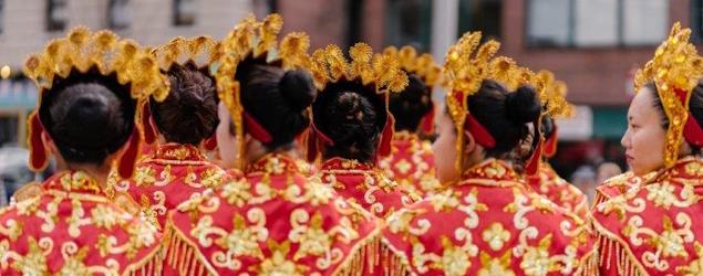 Girls in red and gold costumes and headdresses, shown mostly from behind with a couple in profile (item 194449)