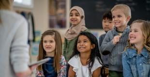 kids sitting and smiling with attention directed to someone holding a book