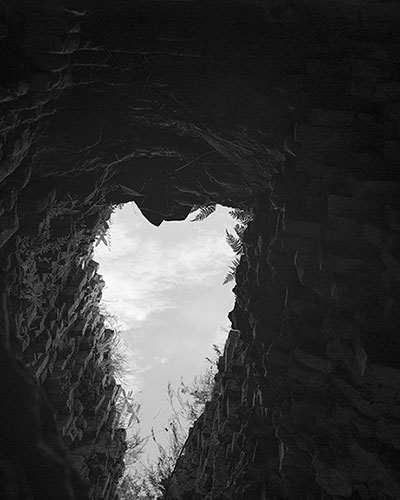 Black and white photo taken from inside a cave, looking outward at a cloudy sky.