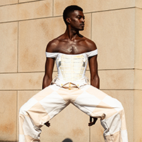 Model Delvin Maleek Whimsical Wheaton wearing a white pleated bustier with checkered cream and tan pants.
