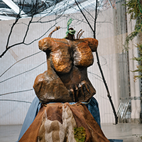 A sculpture of a body's torso on a platform covered in cloth with sticks and foliage surrounding it.