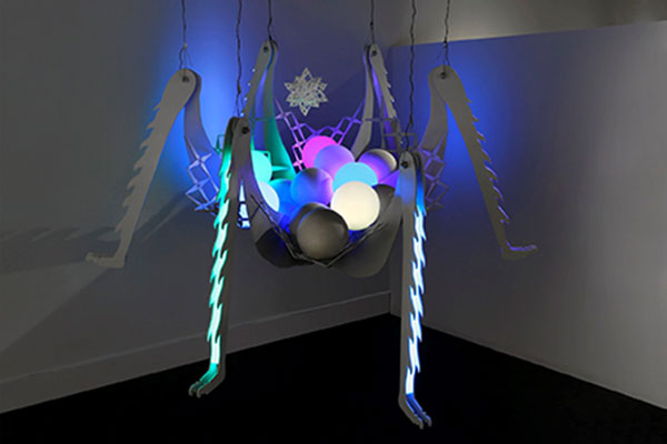 Spider-like sculpture hangs from the ceiling, glowing orbs cradled in it's body.