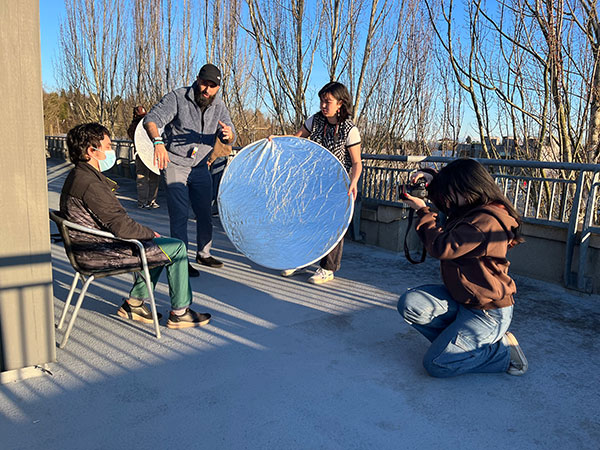 Candid shot of three people working a photo shoot and the subject in a chair.
