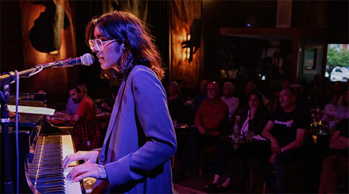 Jahnvi stands at her keyboard, singing into a mic in front of an audience.
