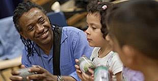 A Black teaching artist leans in and smiles next to two young children.