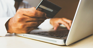 Person holding credit card while typing on laptop