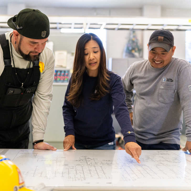 Three City Light employees having a conversation over construction design plans.