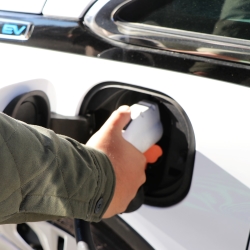 Hand plugging in an electric vehicle charger into a white car.