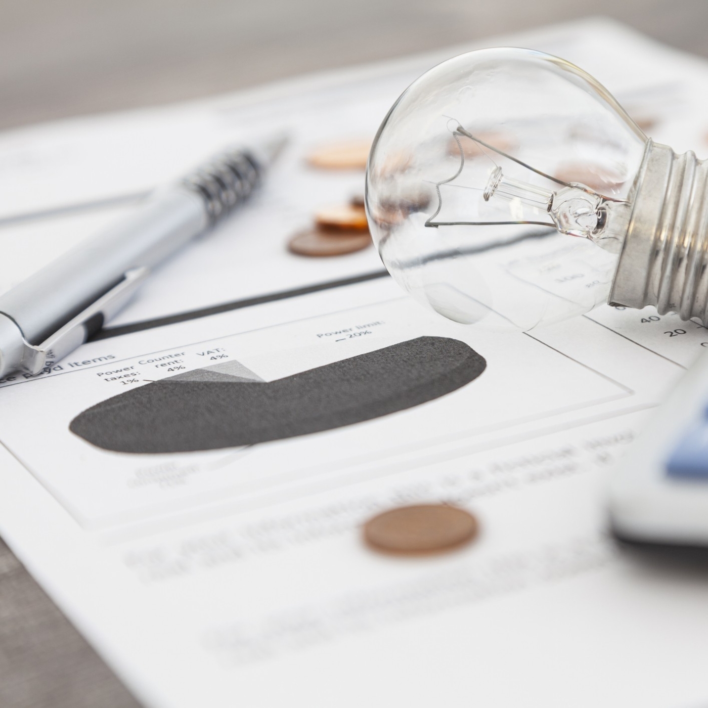 Utility bill laying on table with an ink pen, light bulb, penny, and calculator laying on top of the bill print out.
