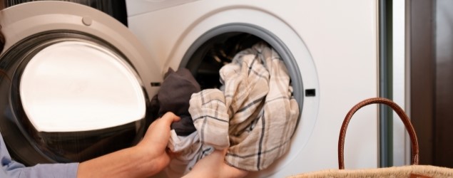 Hands placing a load of laundry into a front loading washing machine.