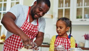 Image depicts an African American father and daughter baking together in a home kitchen. 