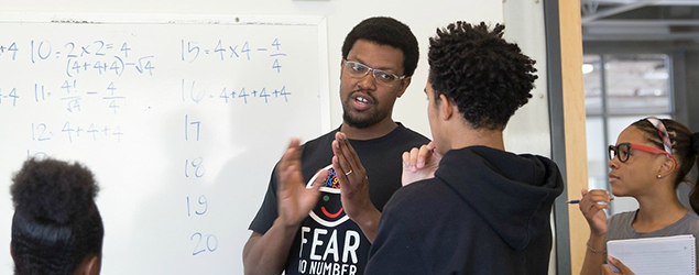a group of students with a teacher, gathered around a whiteboard working on math problems