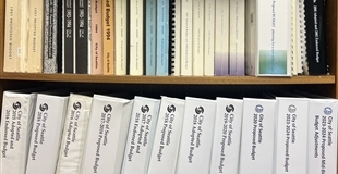 Binders on a bookshelf containing City of Seattle budget books from the 1990s through 2024