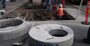 A worker in an orange vest and hardhat working on a road construction site