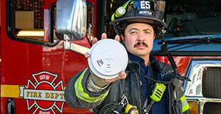 Image of a firefighter holding out a smoke alarm towards camera