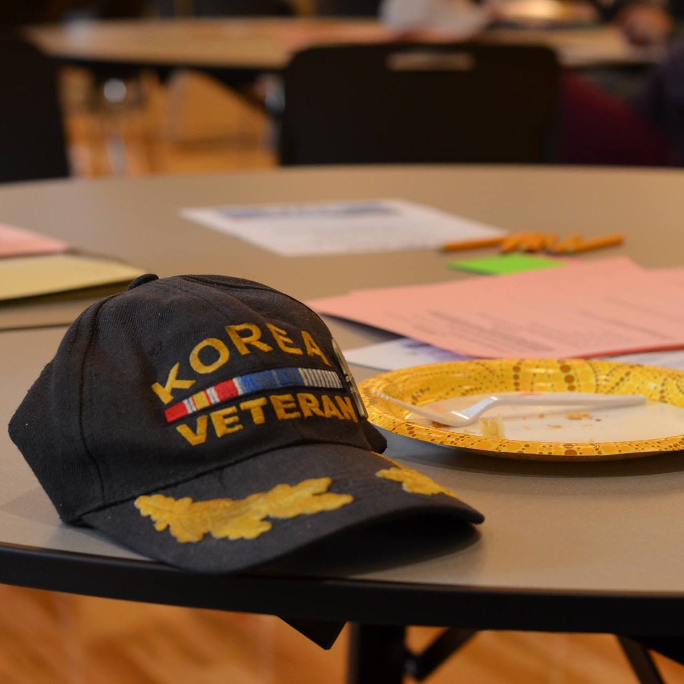 Image of baseball cap with Korean War vet insignias sitting on a table with food and materials