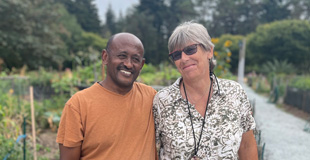 Two people smiling, standing in a lush, green P-Patch Community Garden.