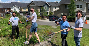 Group of gardeners holding tools and smiling at the camera while working.