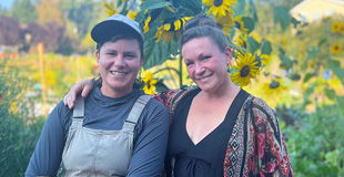 Two gardeners smiling in front a stand of blooming sunflowers.