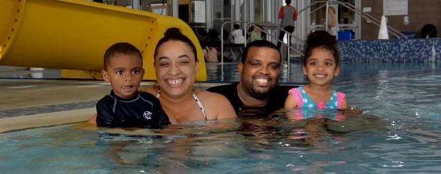 a family of four, two adults and two chlldren, in a swimming pool, posing for the camera.