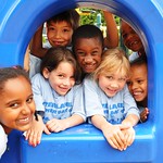several children group together on playground equipment and smile at the camera
