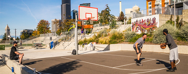 Kids shooting hoops on a basketball court - Smith Tower in the far distance