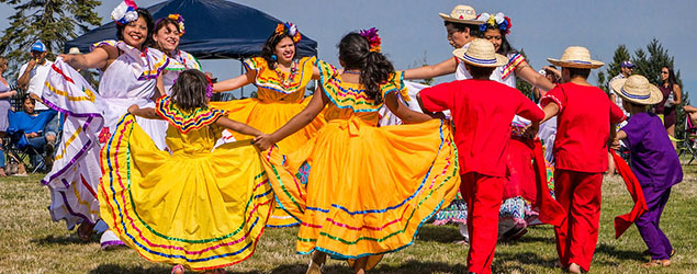 A group of happy, colorfully dressed children dance in a circle