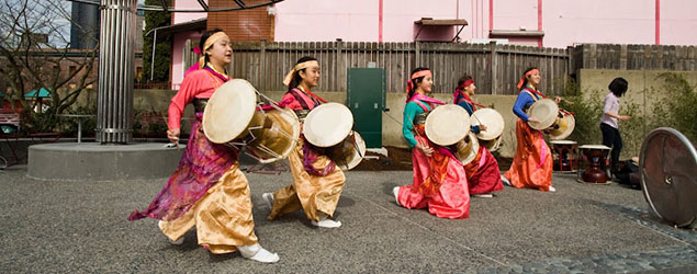 Five festively dressed drummers walking in a line with their drums