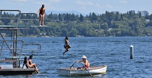Swimmers jumping into a lake from high dive boards on a platform.