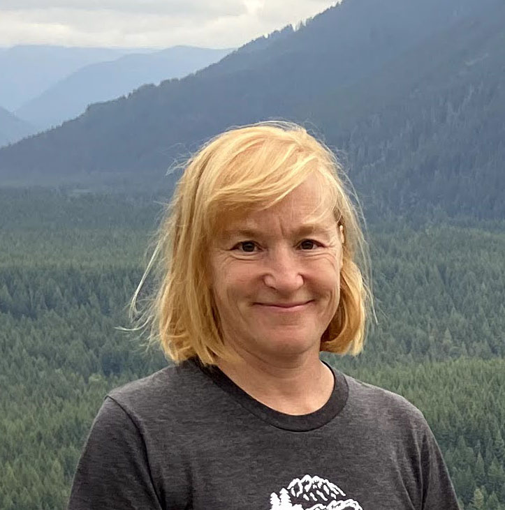 Woman smiling with mountains and trees behind her